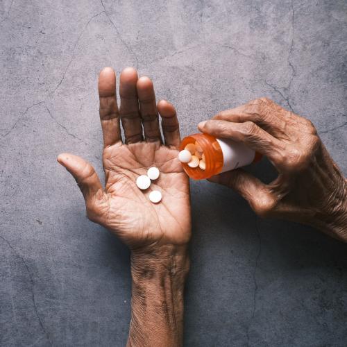 Tabletten werden in die geöffnete Hand eines älteren Menschen gegeben
